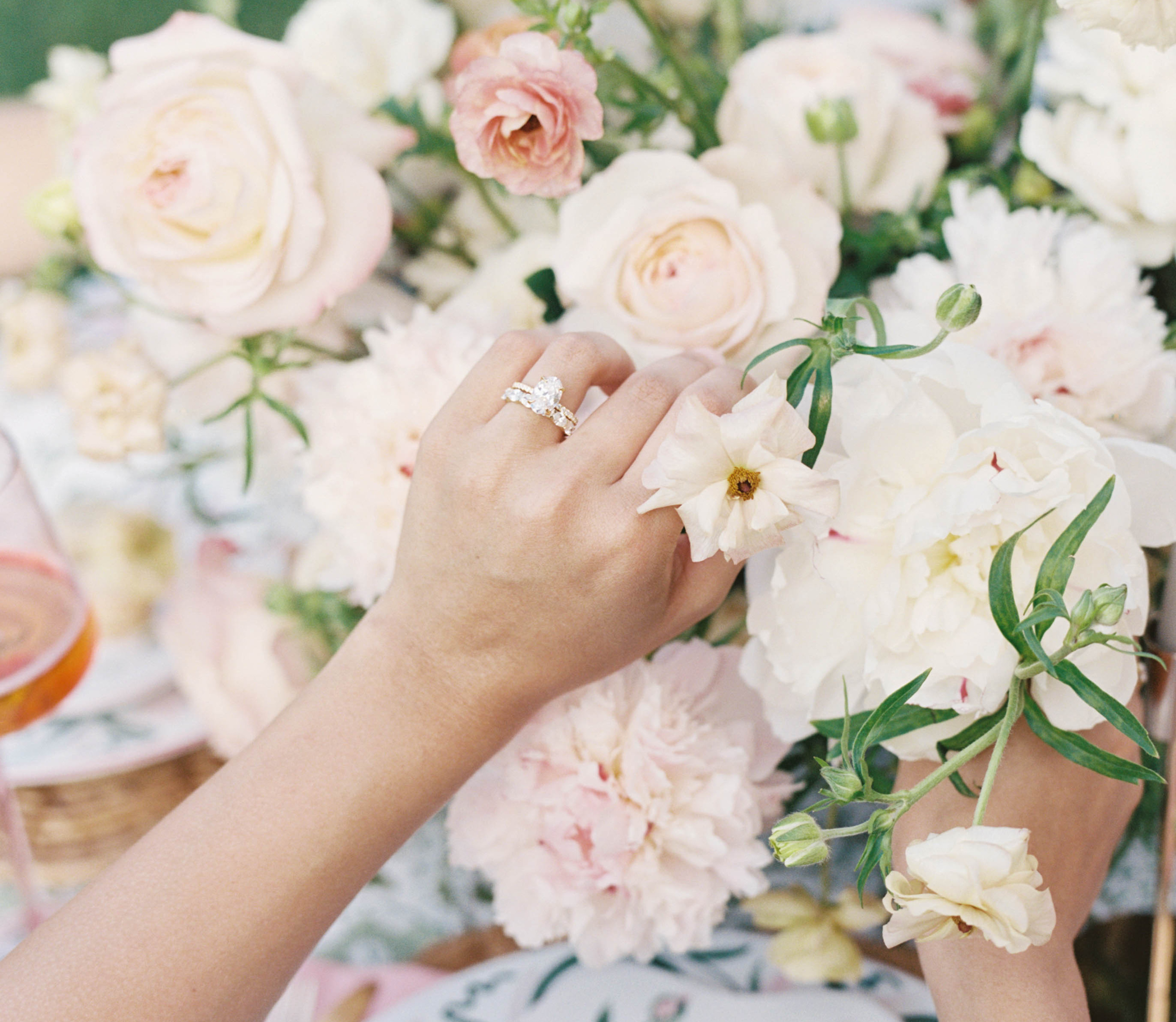 Hand with a ring touching soft pink flowers in a blurred floral background