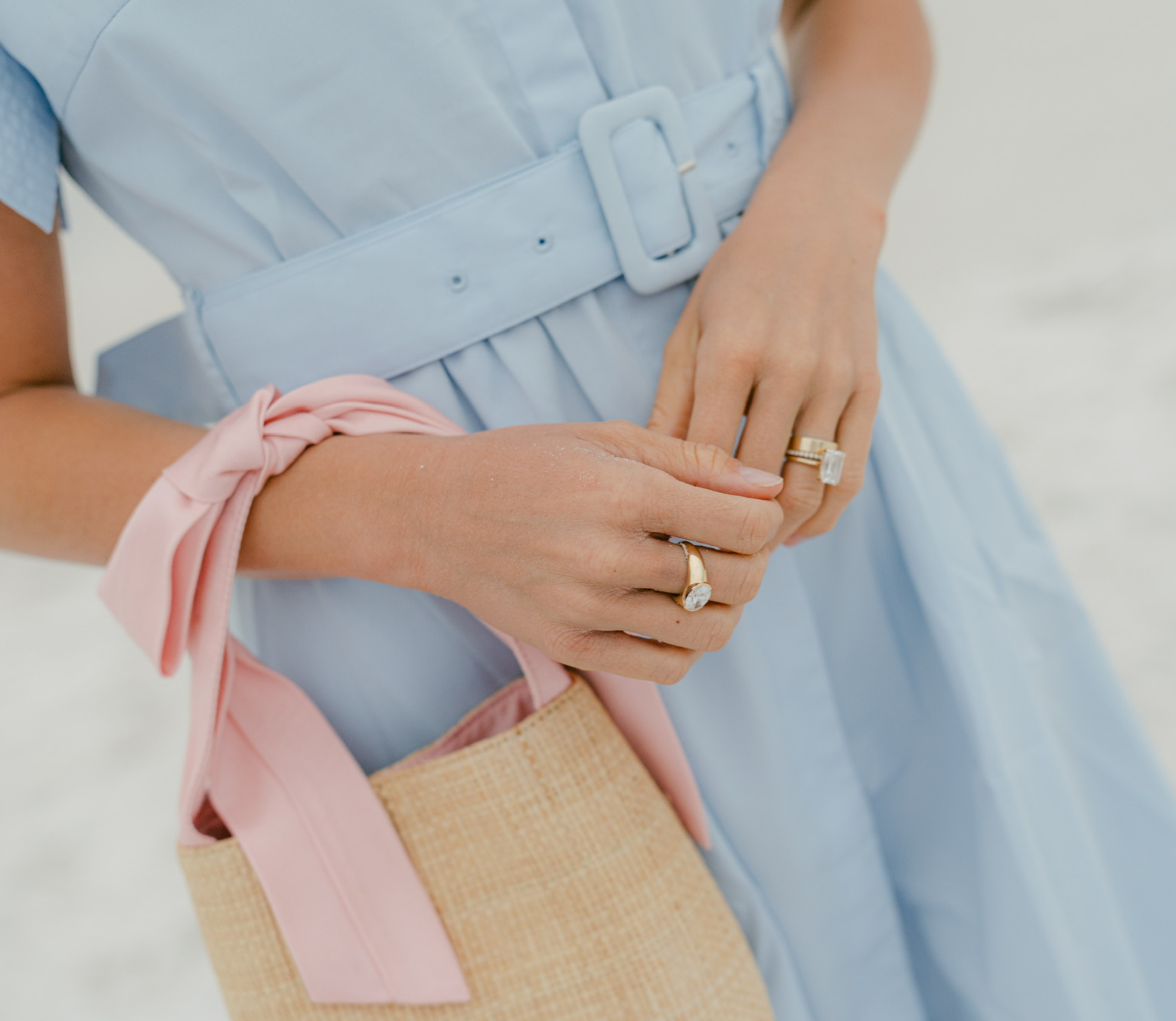 Person wearing a light blue dress with a pink ribbon and holding a woven bag.