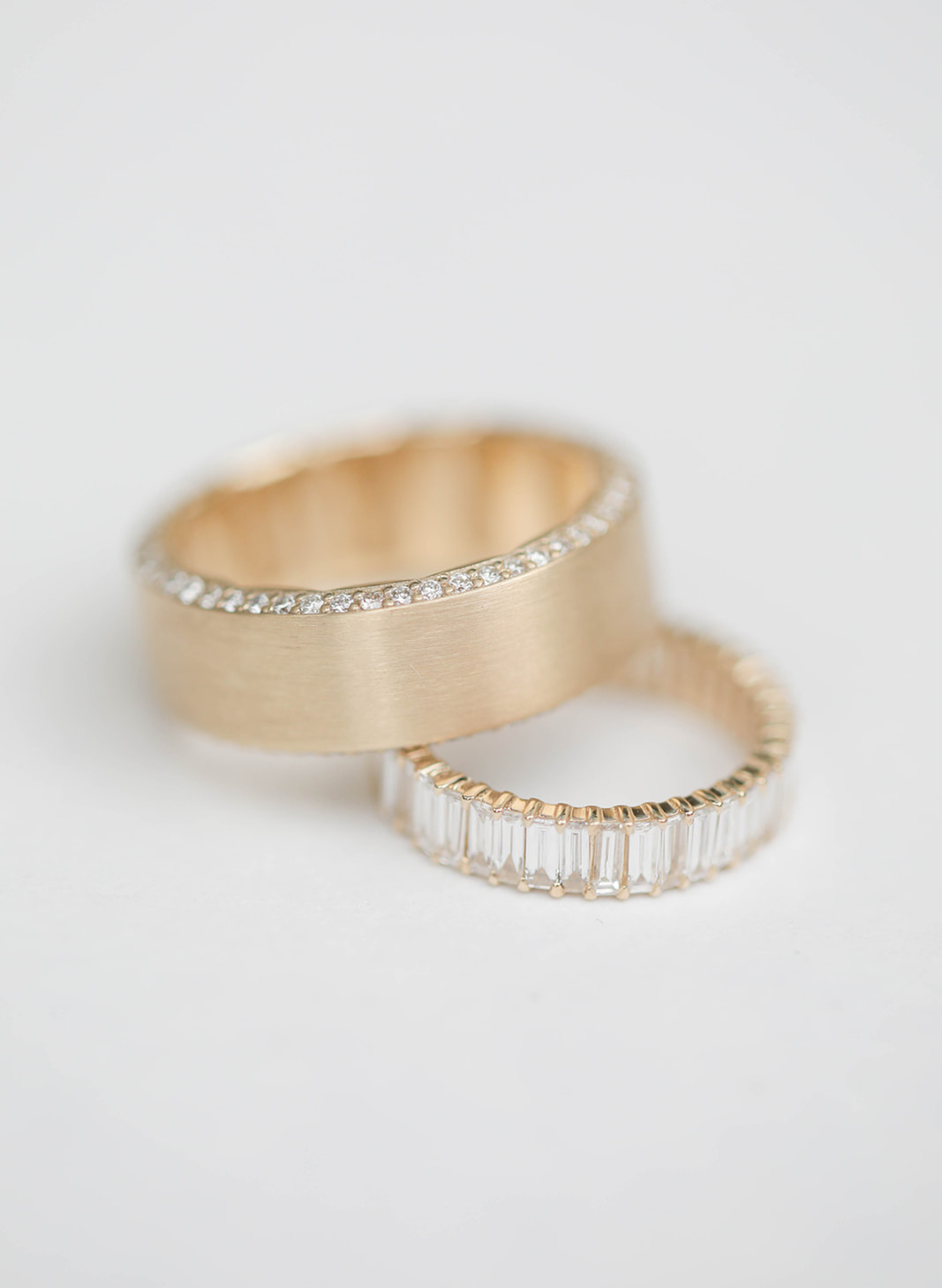 Two gold rings with diamond accents on a light gray background